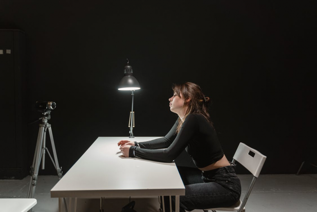 A woman sitting in an interrogation room with a camera pointed at her